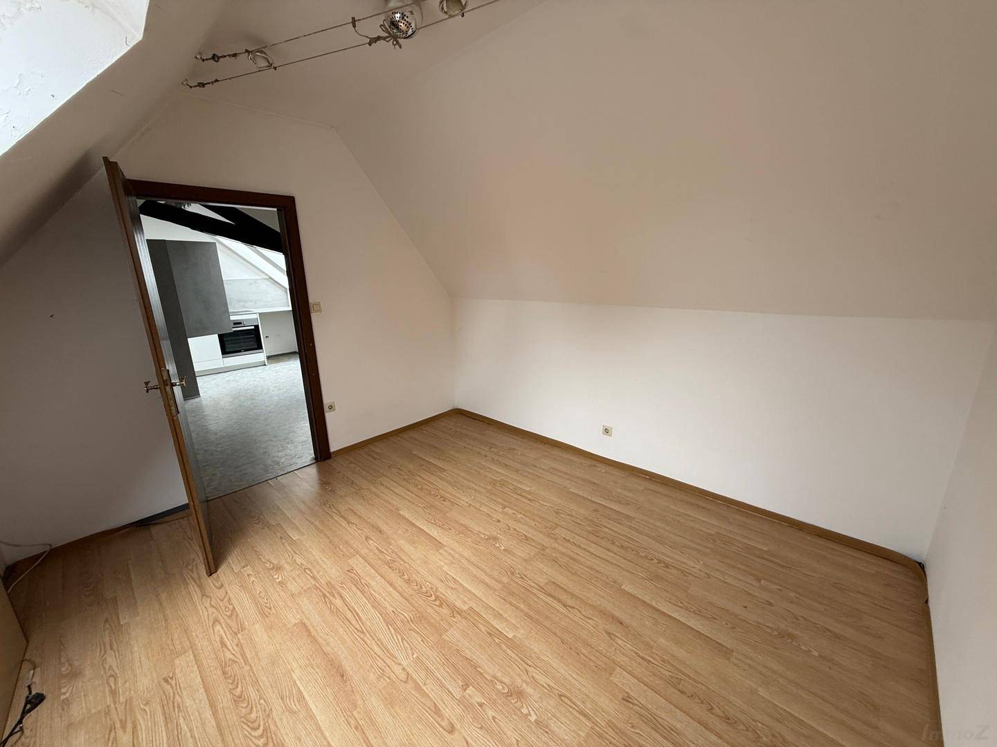 Schlafzimmer im Dachgeschoss mit Laminatboden und Blick in die angrenzende Küche.