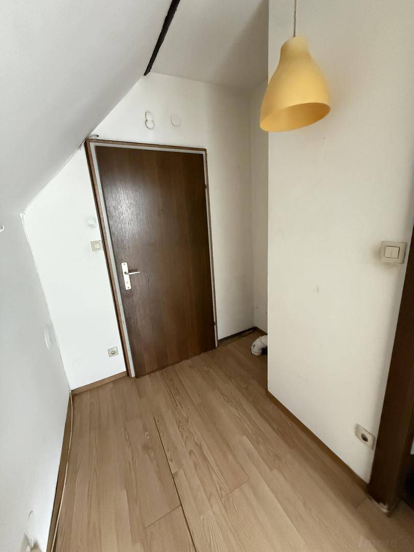 Eingangsbereich im Dachgeschoss mit Laminatboden, weiß gestrichenen Wänden und einer Holztür.