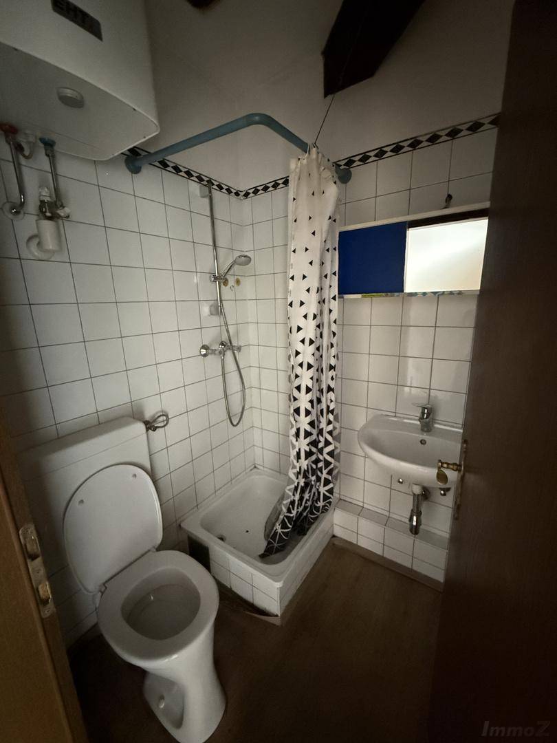 Kleines Badezimmer mit Dusche, WC und Waschbecken, ausgestattet mit weißen Fliesen und einem Fenster.