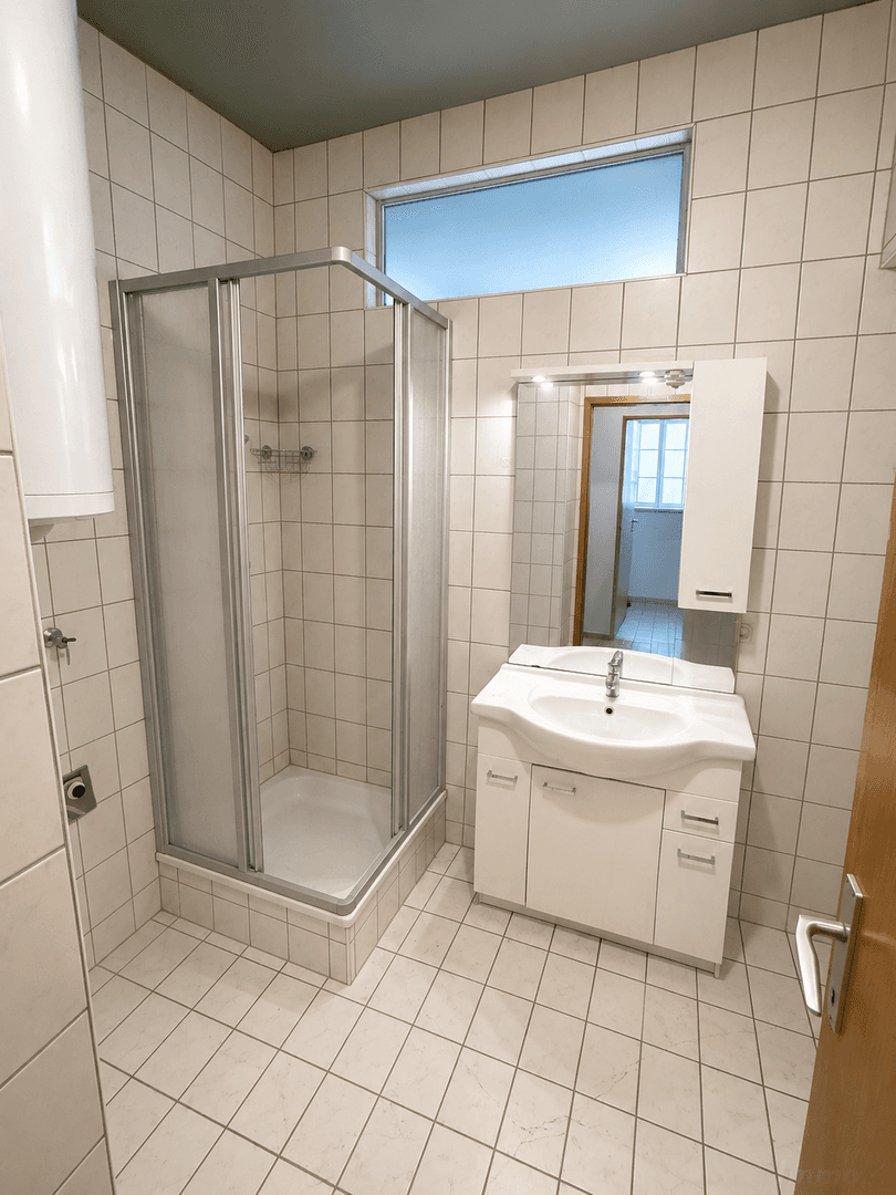 Funktionales Badezimmer mit Duschkabine, Einzelwaschbecken und Fliesen an Wänden und Boden.