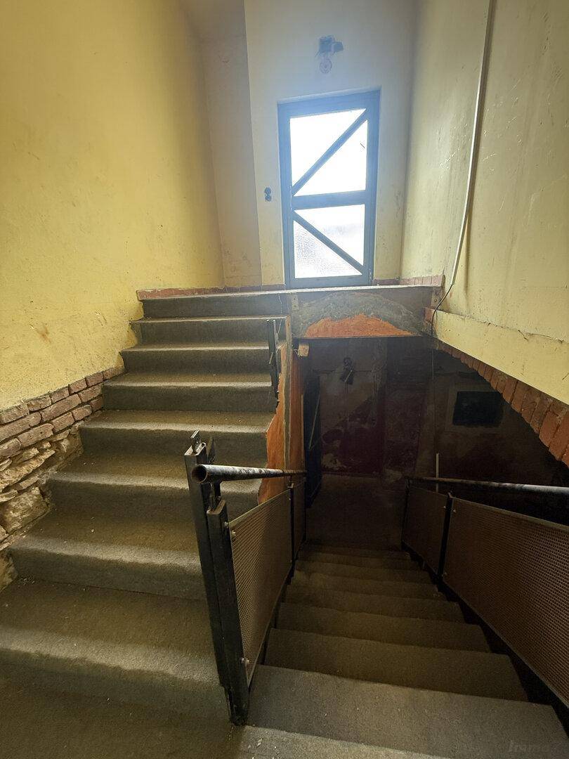 Alter Treppenaufgang mit Betonstufen, gelben Wänden und sichtbaren Ziegeln, der nach oben und unten führt.