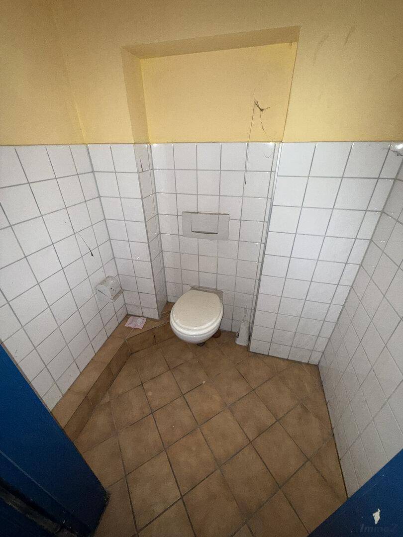 Toilettenkabine mit WC, weißen Fliesen an den Wänden und braunen Fliesen auf dem Boden.