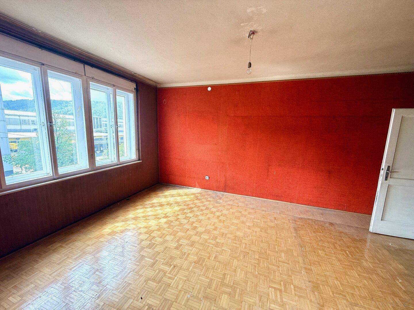 Helles Wohnzimmer mit roter Wand und Fischgrätparkett, das viel Tageslicht erhält.