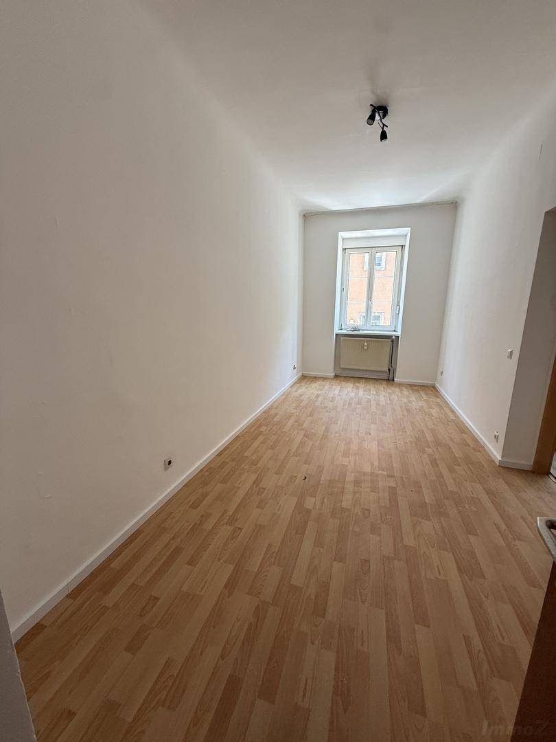 Heller, leerer Raum mit weißen Wänden und Laminatboden, ideal als Wohn- oder Schlafzimmer.