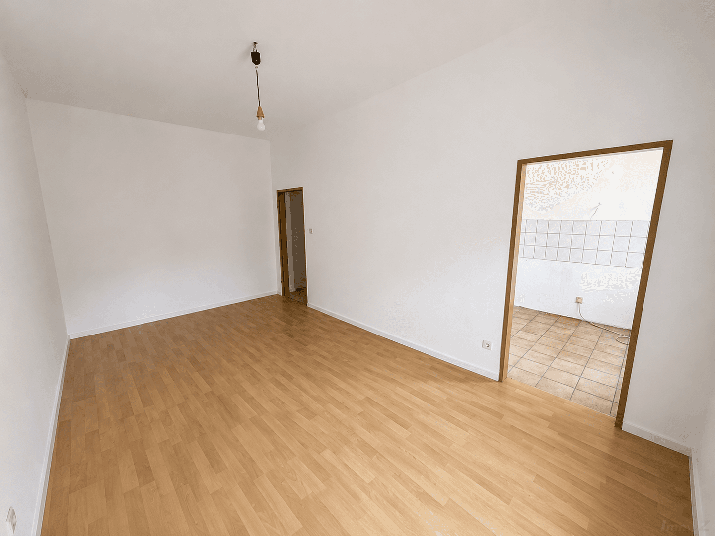 Geräumiges, helles Zimmer mit Laminatboden und Zugang zu einem weiteren Raum mit Fliesen.