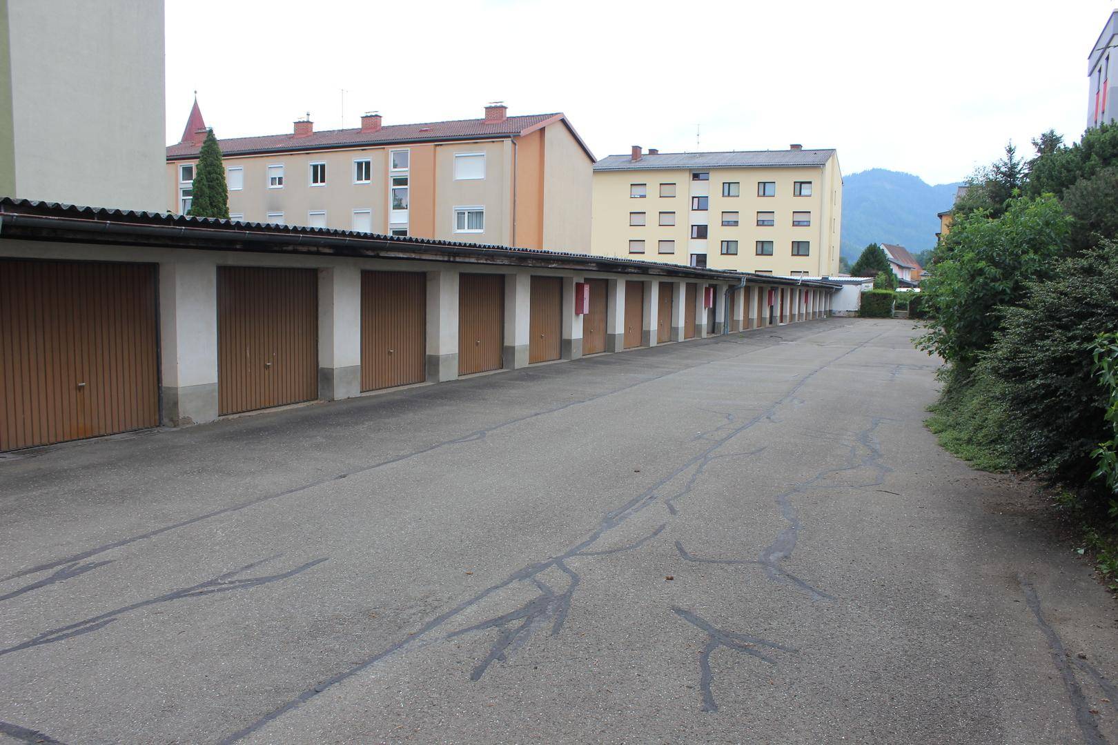 Reihe von Garagenboxen mit asphaltiertem Vorplatz und Mehrfamilienhäusern im Hintergrund.