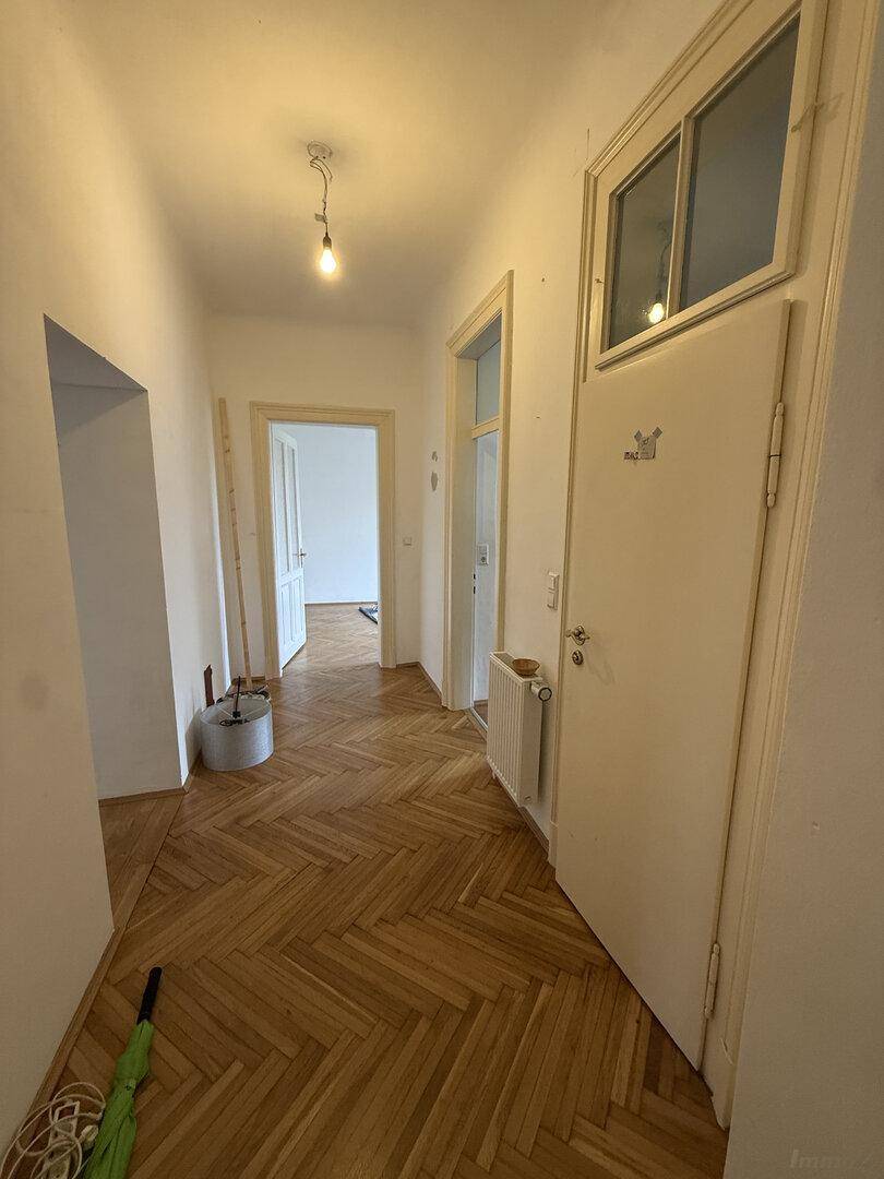 Heller Flur mit Fischgrätparkett, Heizkörper und einer Tür mit Oberlicht, die zu weiteren Räumen führt.