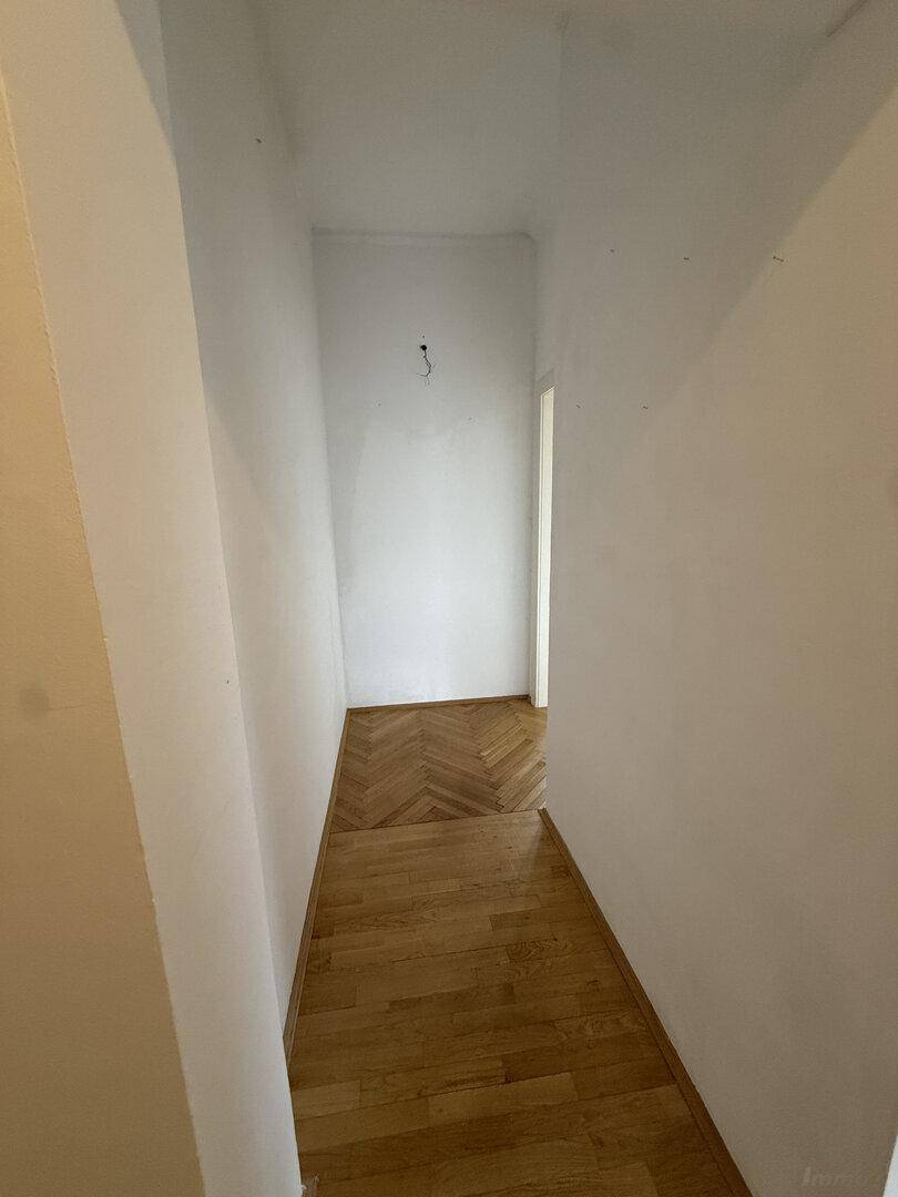 Schmaler Flur mit hellem Parkettboden und weißen Wänden, der zu einem weiteren Bereich führt.