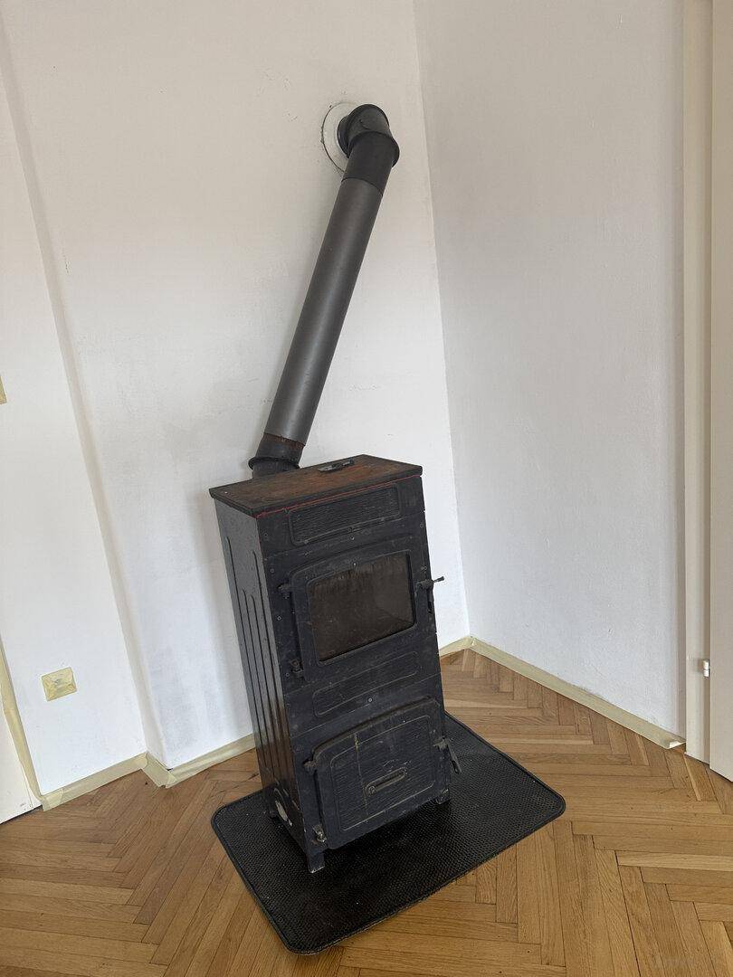 Detailansicht eines schwarzen Holzofens mit Rauchrohr auf dem Fischgrätparkett.