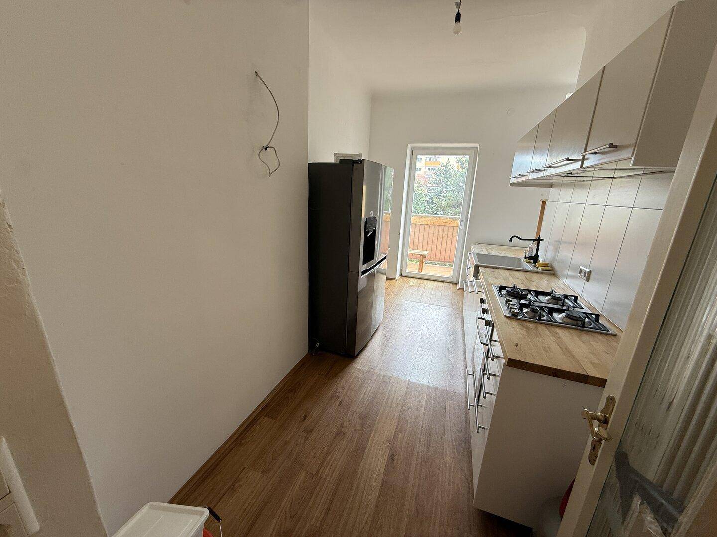 Funktionale Küche mit weißen Schränken, Holz-Arbeitsplatte, Gasherd und Zugang zum Balkon.