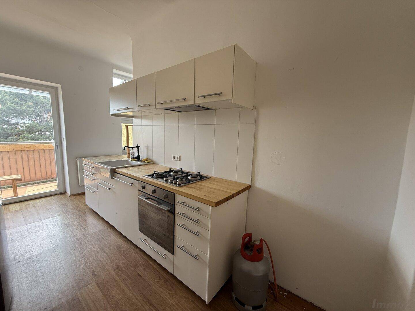 Helle Küche mit weißen Unterschränken, Holz-Arbeitsplatte, Gasherd und direktem Balkonzugang.