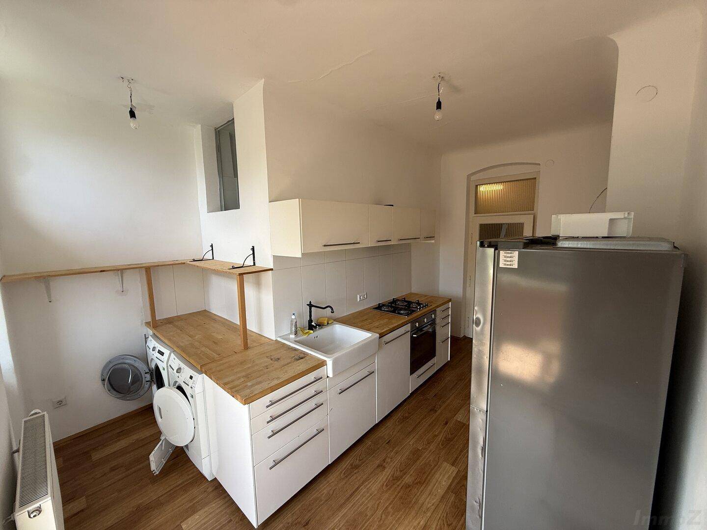 Praktische Küche mit weißen Schränken, Holz-Arbeitsplatte, Kühlschrank und integrierter Waschmaschine.