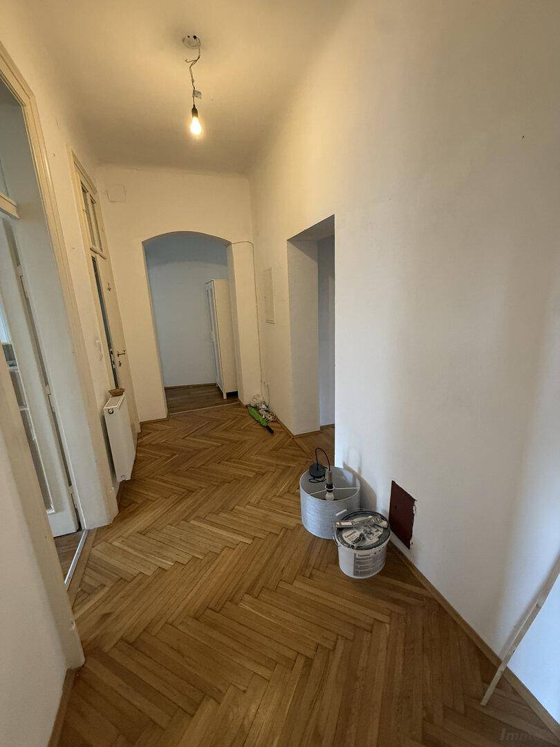 Heller Flur mit Fischgrätparkett und einem eleganten Bogen, der auf eine Renovierung hindeutet.