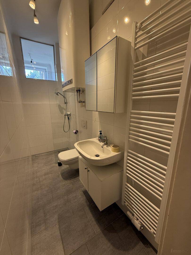 Modernes Badezimmer mit weißen Wandfliesen, grauen Bodenfliesen, Dusche und Handtuchheizkörper.