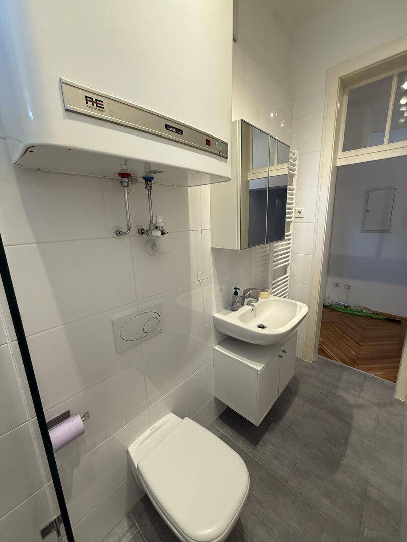 Modernes Badezimmer mit Wand-WC, Waschbecken, Spiegelschrank und beheiztem Handtuchhalter.