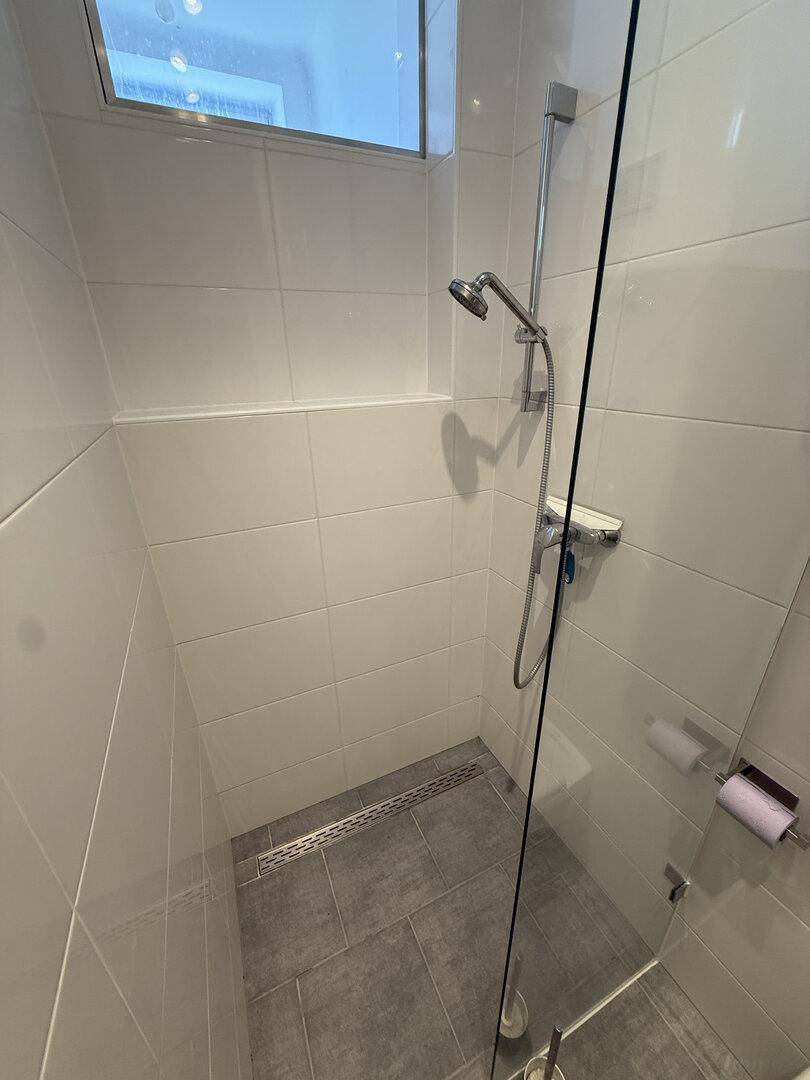 Detaillierte Ansicht der modernen Dusche mit Glasabtrennung und grauen Bodenfliesen.