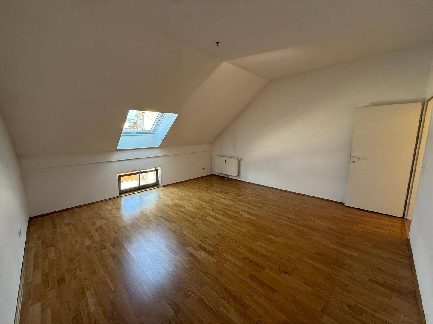Geräumiges Zimmer im Dachgeschoss mit Holzboden und einem Dachfenster, das den Raum erhellt.