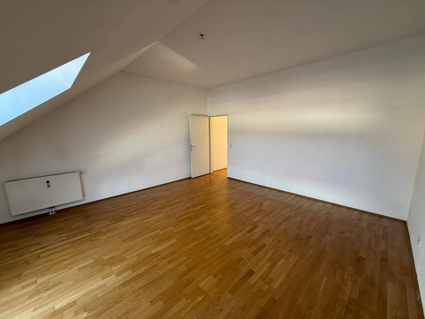 Lichtdurchflutetes Dachzimmer mit Holzboden und Zugang zu einem weiteren Raum, ideal als Schlafzimmer.