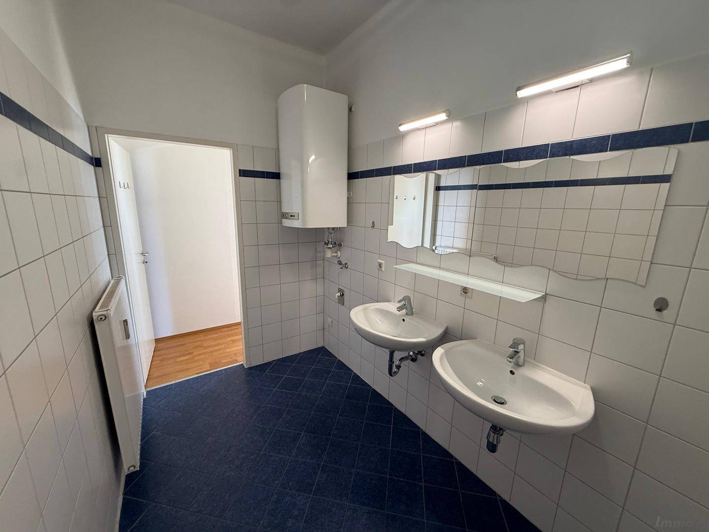 Geräumiges Badezimmer mit Doppelwaschbecken, großem Spiegel und weiß-blauen Fliesen.