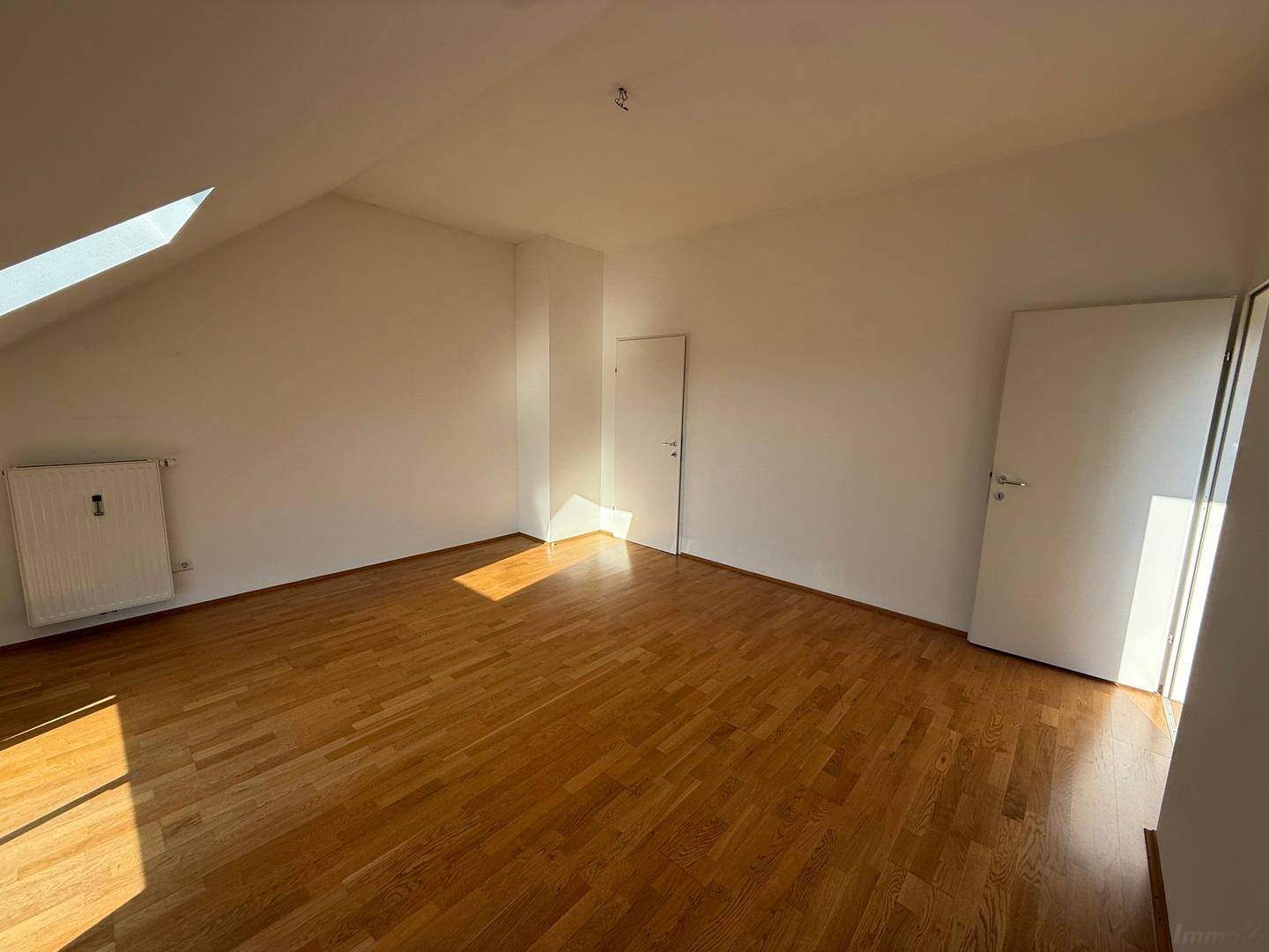 Lichtdurchflutetes Dachzimmer mit Holzboden und Zugang zu einem weiteren Raum, ideal als Schlafzimmer.