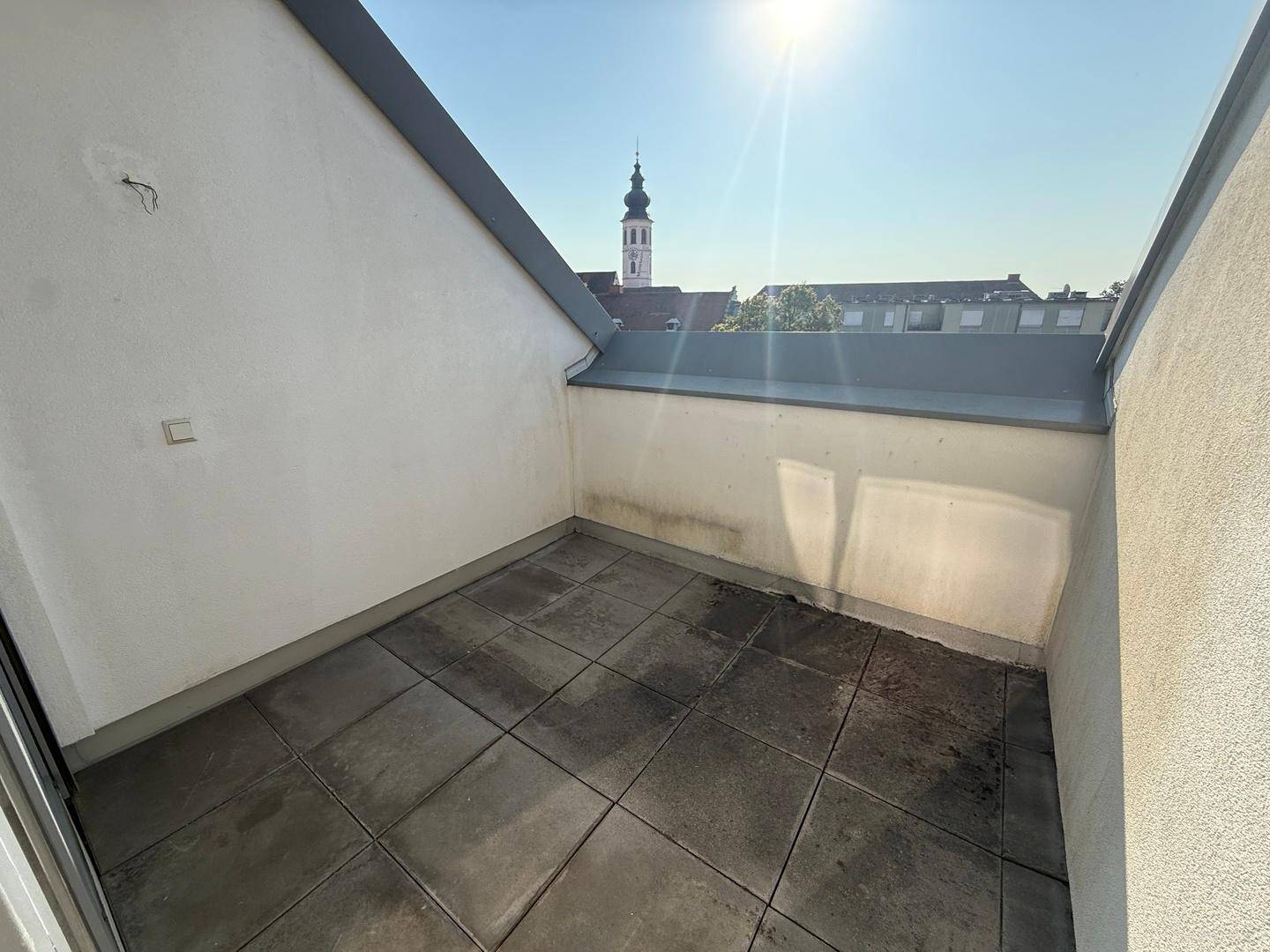 Sonniger Außenbereich mit Fliesenboden und Blick auf einen Kirchturm sowie die umliegende Stadt.