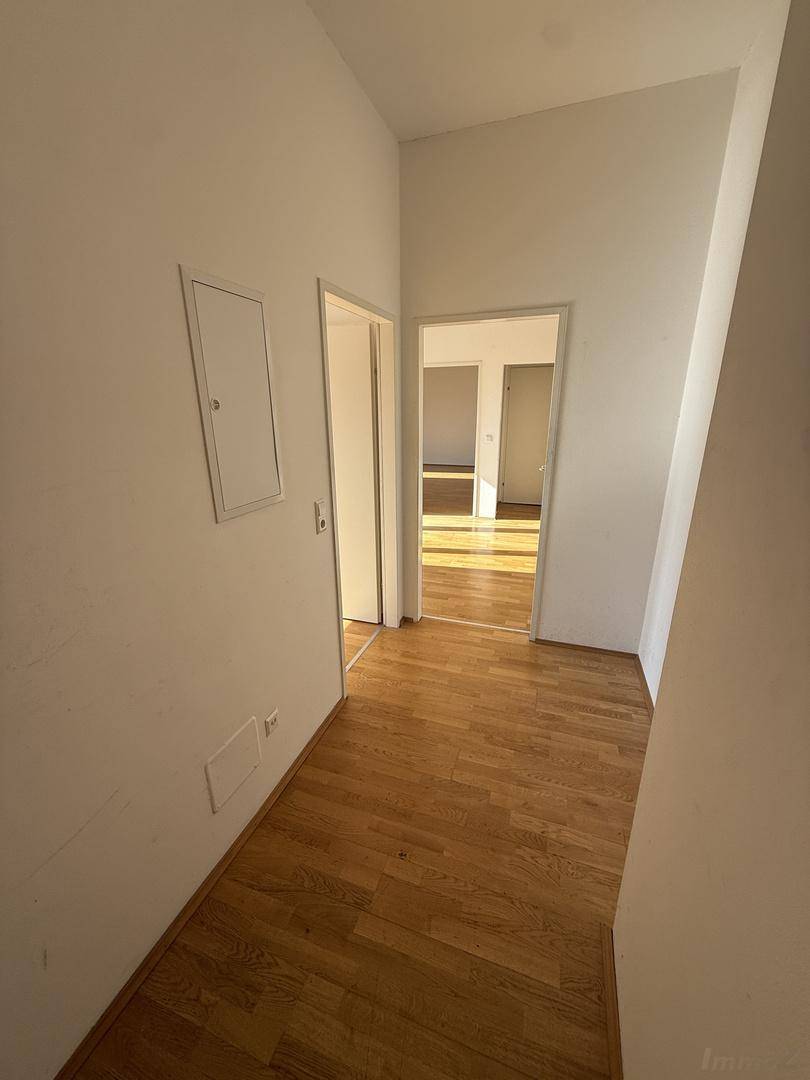 Heller Flur mit Holzboden, weißen Wänden und offenen Türen zu angrenzenden Räumen.