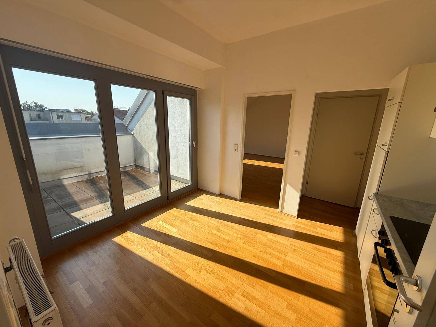 Heller Wohnbereich mit Holzboden und großen Glasschiebetüren, die auf eine sonnige Terrasse führen.