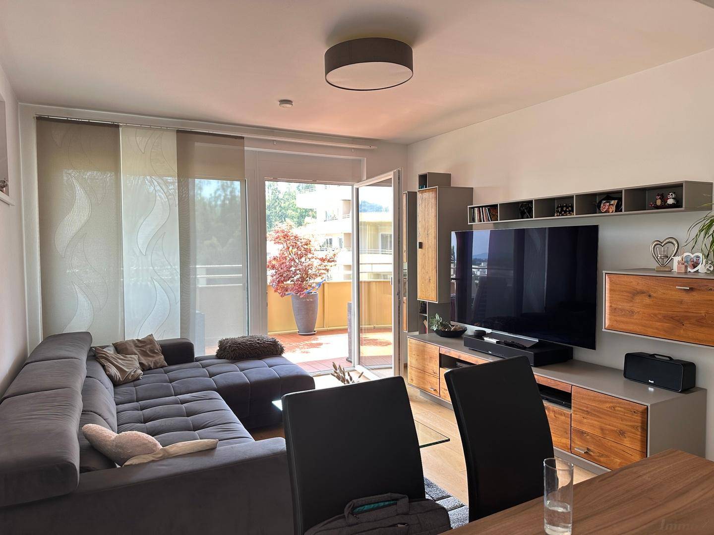 Gemütliches Wohnzimmer mit großem Sofa, TV-Möbeln und Zugang zum sonnigen Balkon.