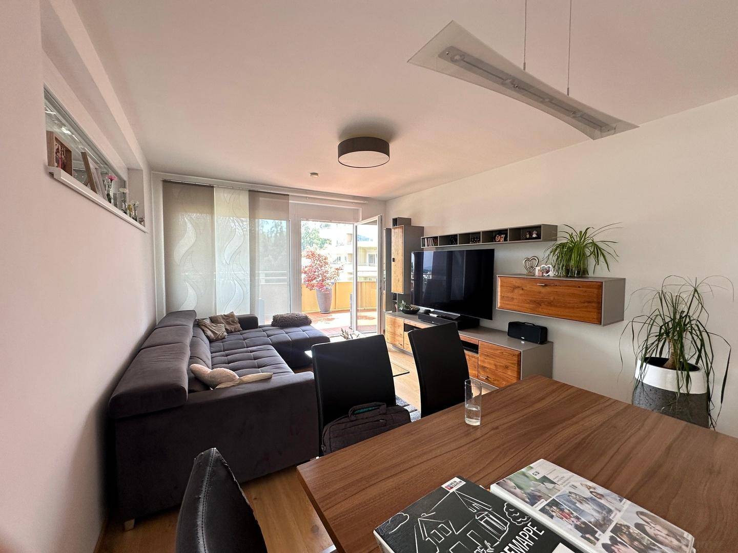 Moderner Wohn-Essbereich mit Holzboden, Esstisch und Sofa, mit Zugang zum Balkon.
