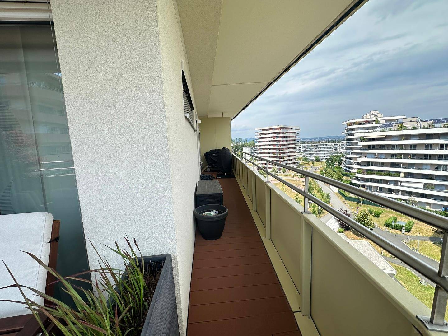 Balkon mit Pflanzen, einem abgedeckten Grill und weitem Blick auf die moderne Wohnsiedlung.