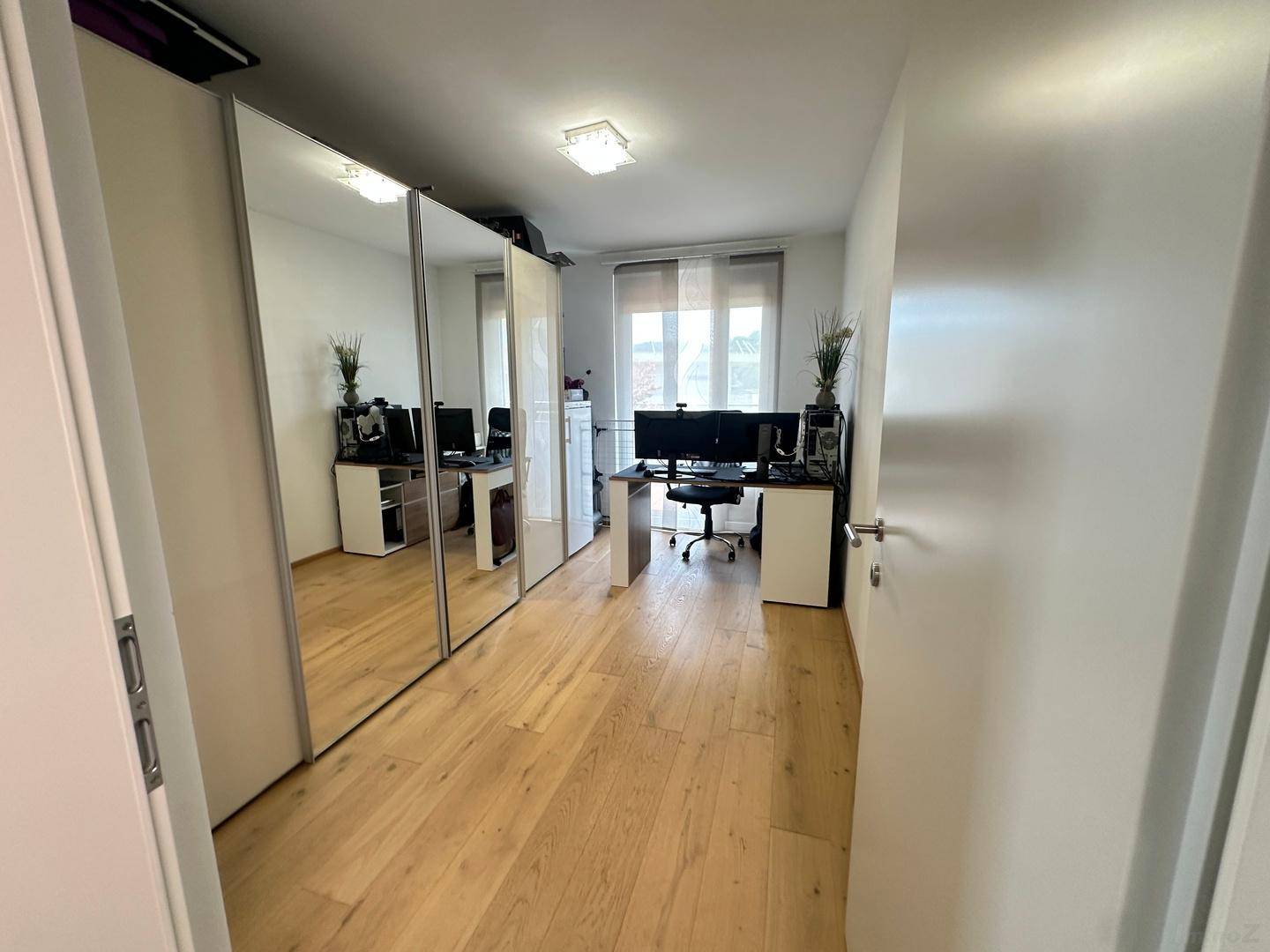 Helles Arbeitszimmer mit Holzboden, Spiegelschränken und Blick nach draußen.
