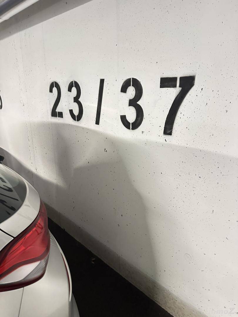 Parkplatznummer 23/37 an einer weißen Wand in einer Tiefgarage mit einem geparkten Auto.