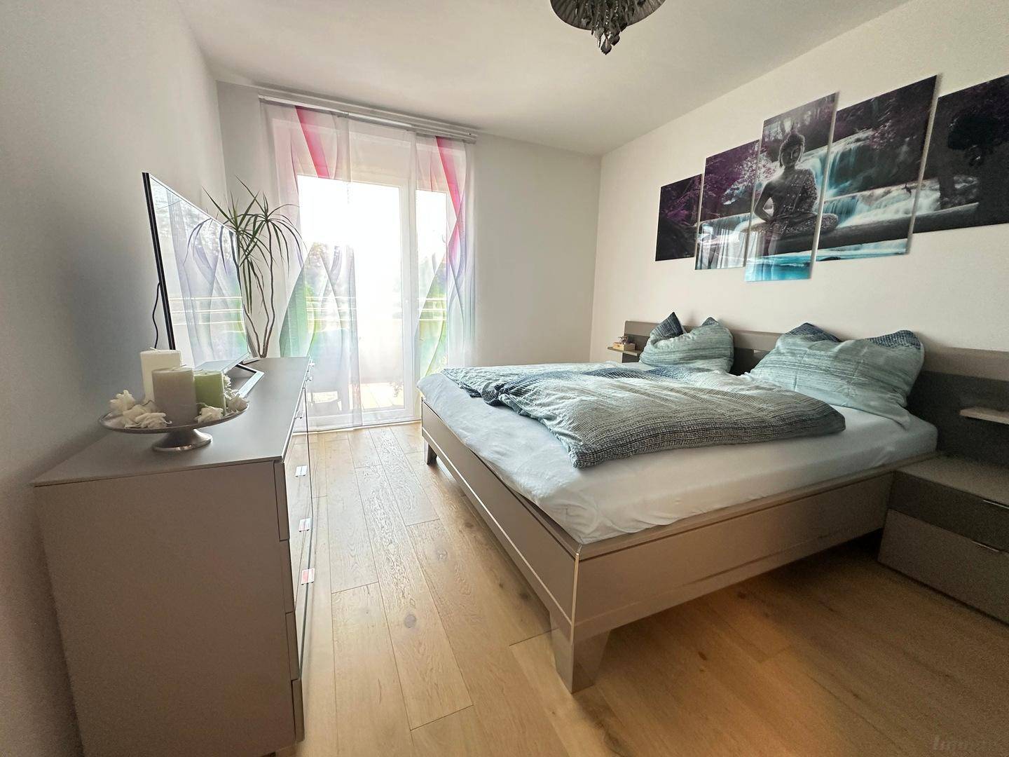 Helles Schlafzimmer mit Holzboden, Doppelbett und Zugang zum Balkon.