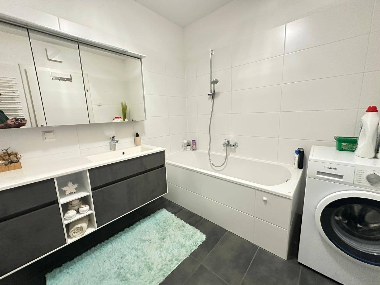 Funktionales Badezimmer mit Waschtisch, Spiegelschrank, Badewanne und integrierter Waschmaschine.