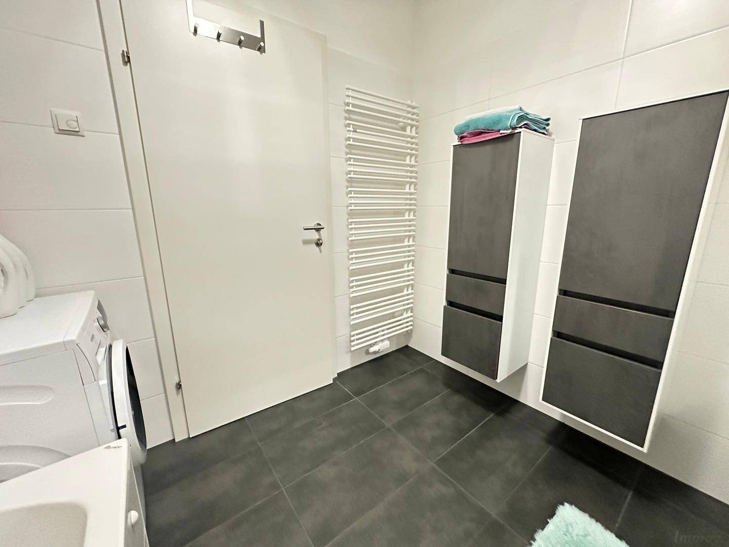 Badezimmer mit modernem Handtuchheizkörper und praktischen Hängeschränken über dunklen Fliesen.