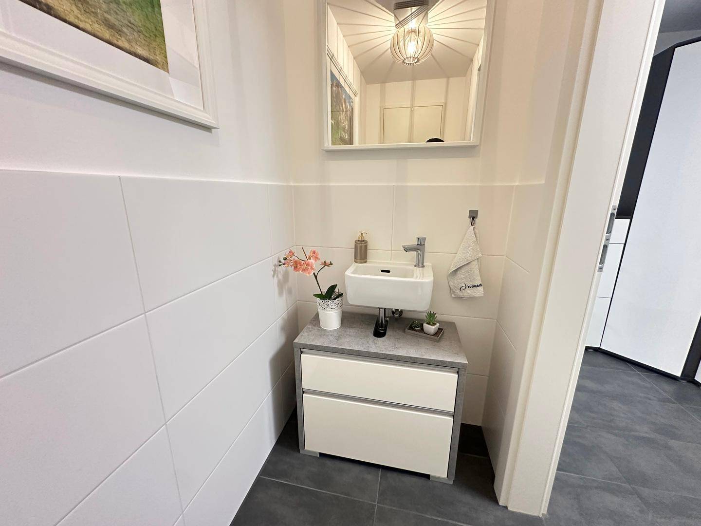 Kleines Gäste-WC mit modernem Waschtisch, Spiegel und dekorativer Orchidee.