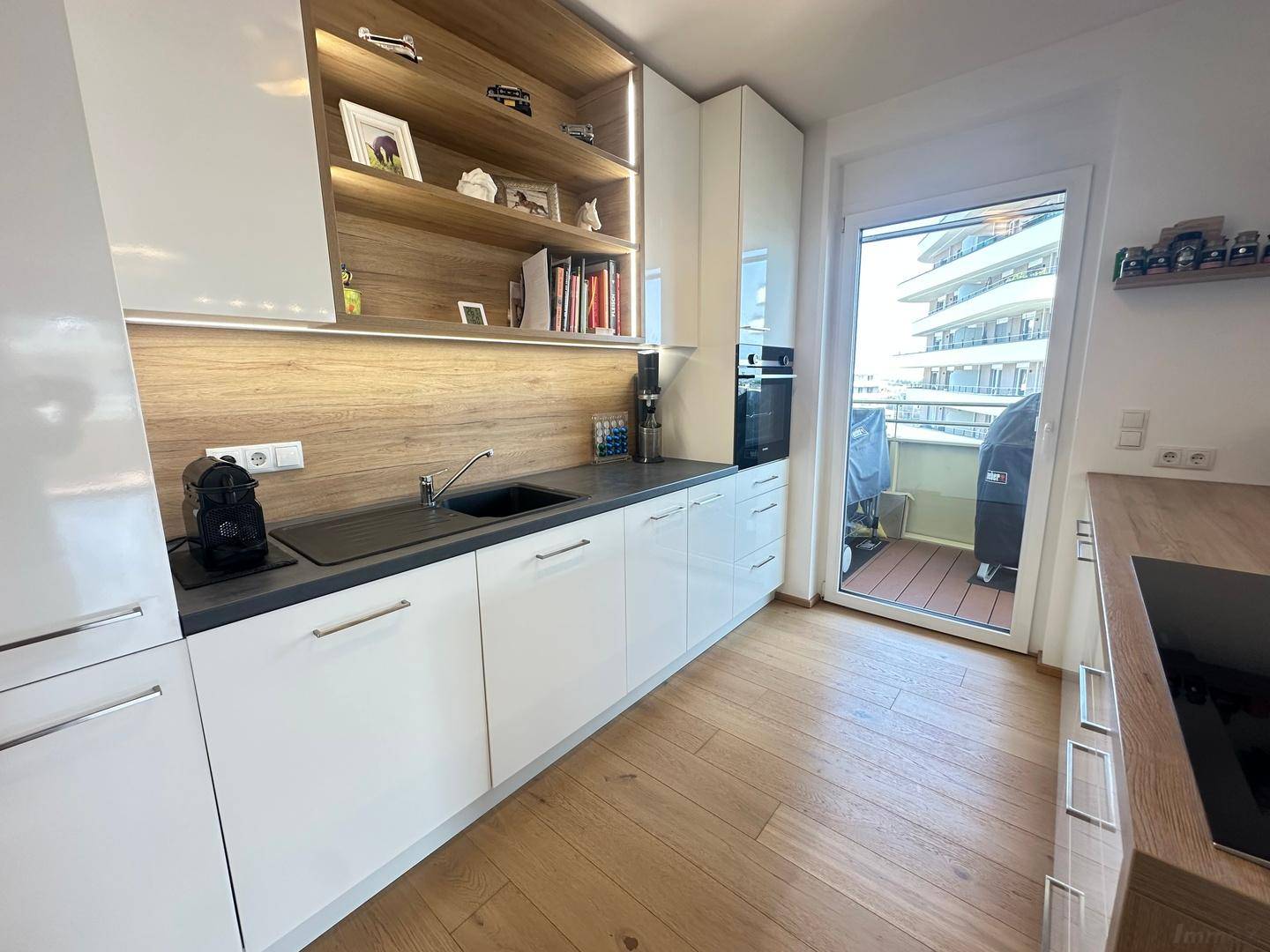 Stilvolle Küche mit weißen Schränken, dunkler Arbeitsplatte und Zugang zum Balkon.
