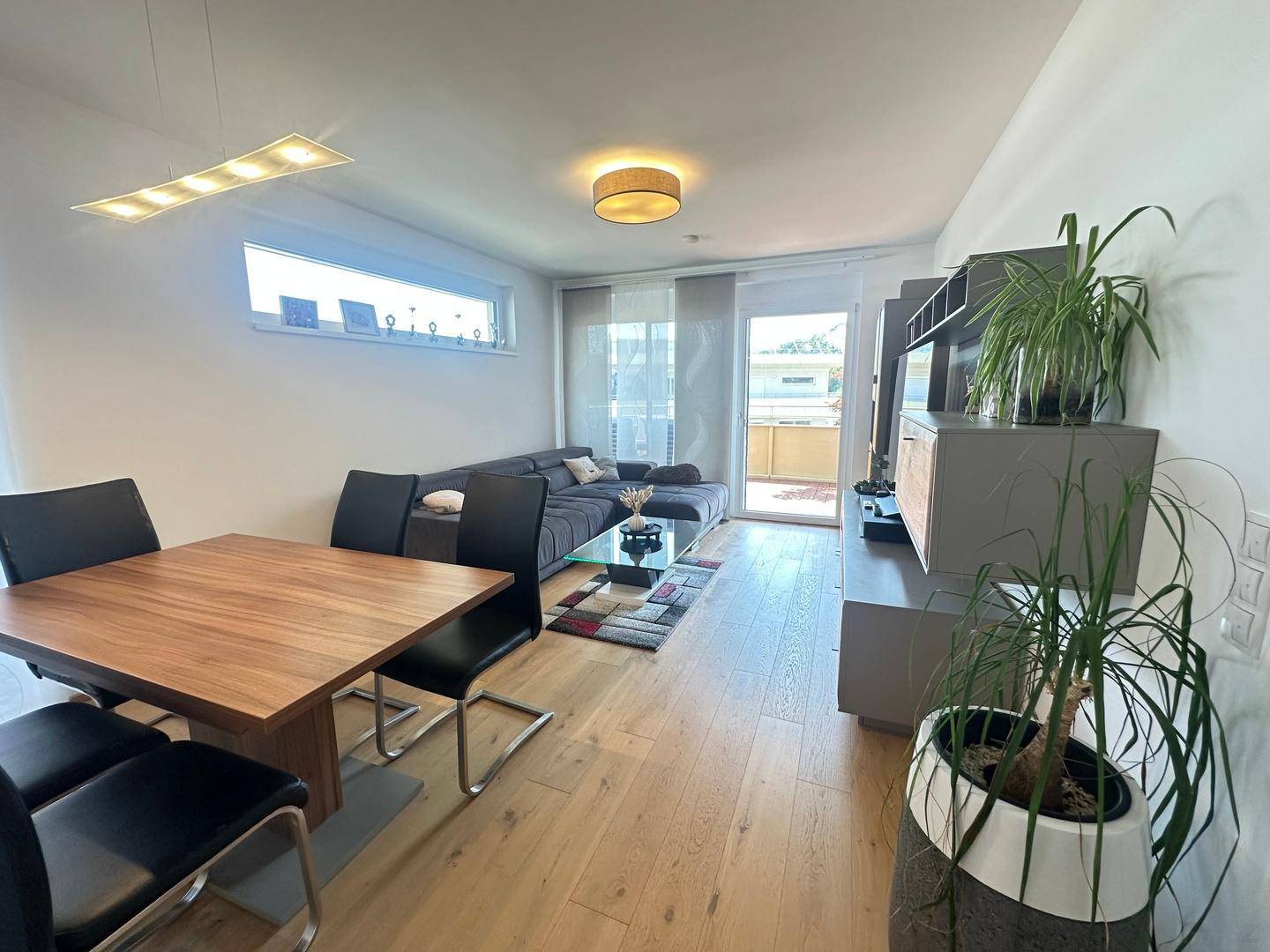 Geräumiger Wohn-Essbereich mit Holzboden, großem Esstisch und gemütlichem Sofa.