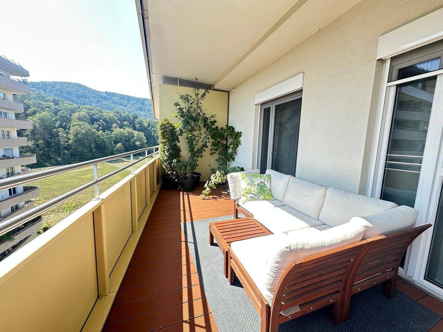 Langer Balkon mit bequemen Outdoor-Möbeln und weitem Blick auf die grüne Landschaft.