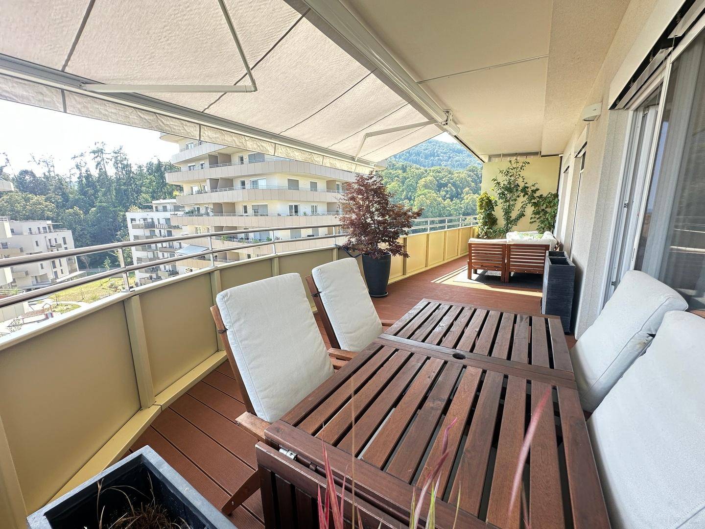 Geräumiger Balkon mit Holztisch, Stühlen, Markise und weitem Blick auf die Umgebung und Berge.
