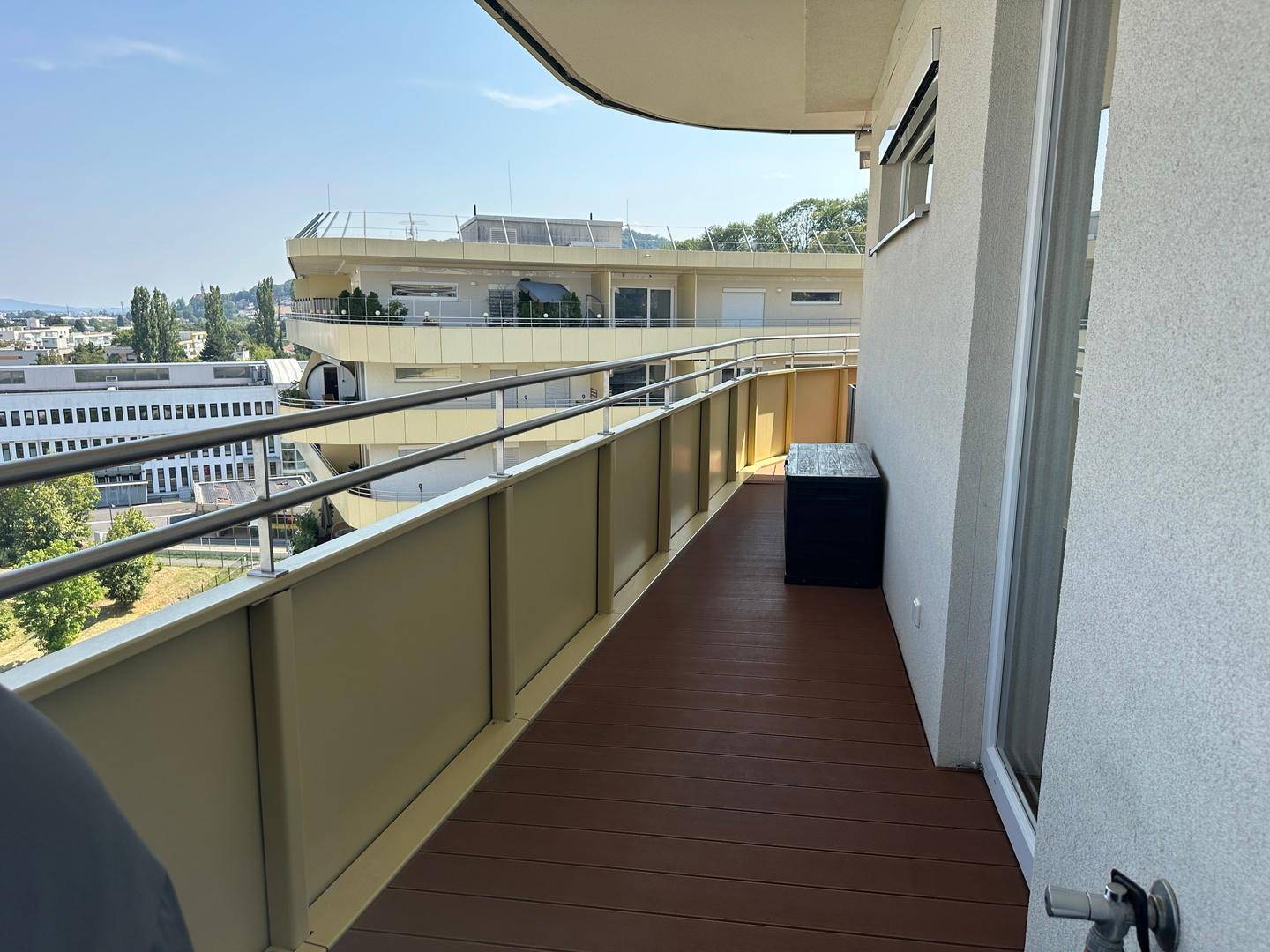 Schmaler Balkon mit einer Aufbewahrungsbox und Blick auf die umliegende moderne Architektur.