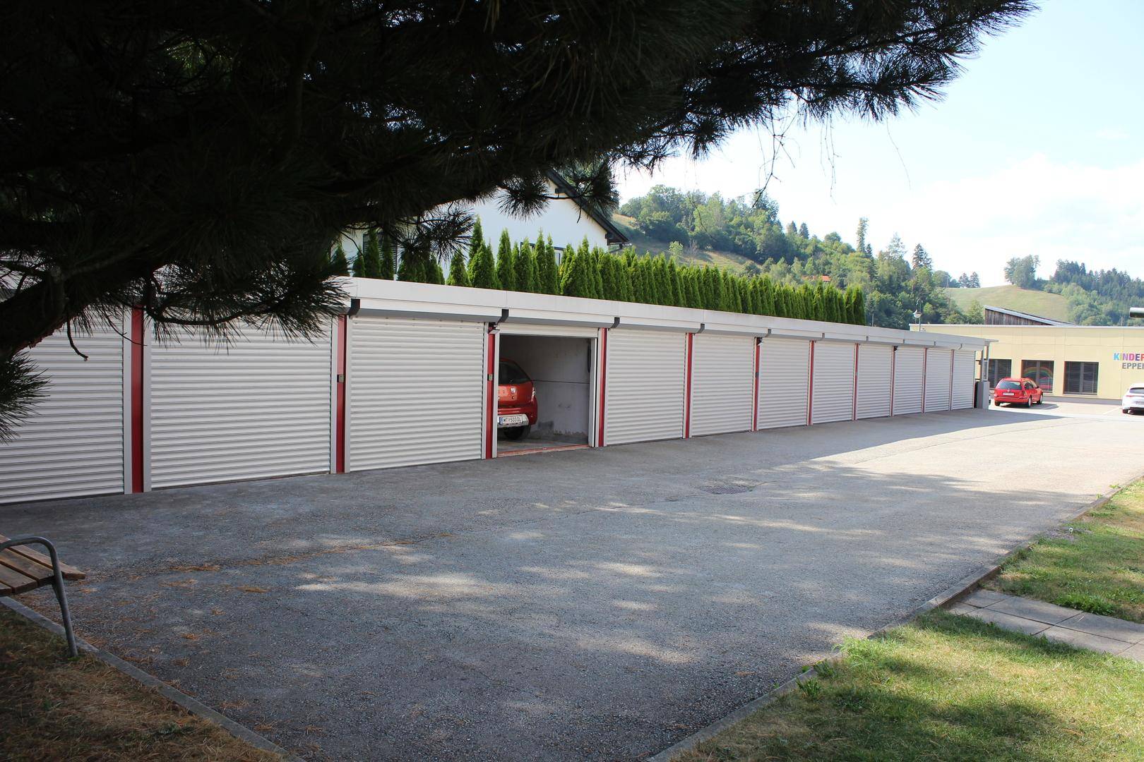Reihe von Garagen mit Rolltoren und einem roten Auto in einer geöffneten Garage.