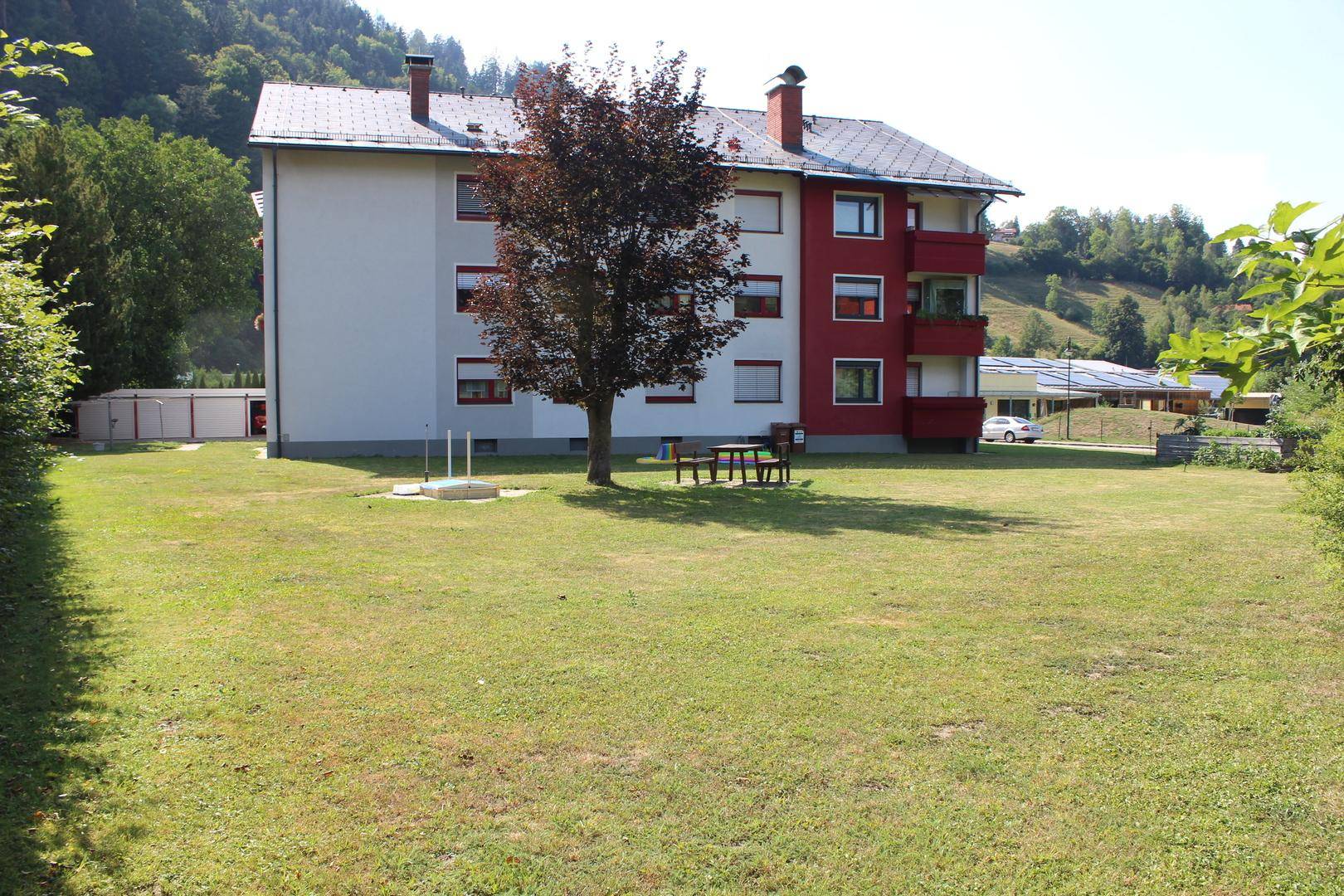 Großer Gemeinschaftsgarten hinter dem Mehrfamilienhaus mit Sitzgelegenheit und viel Grünfläche.