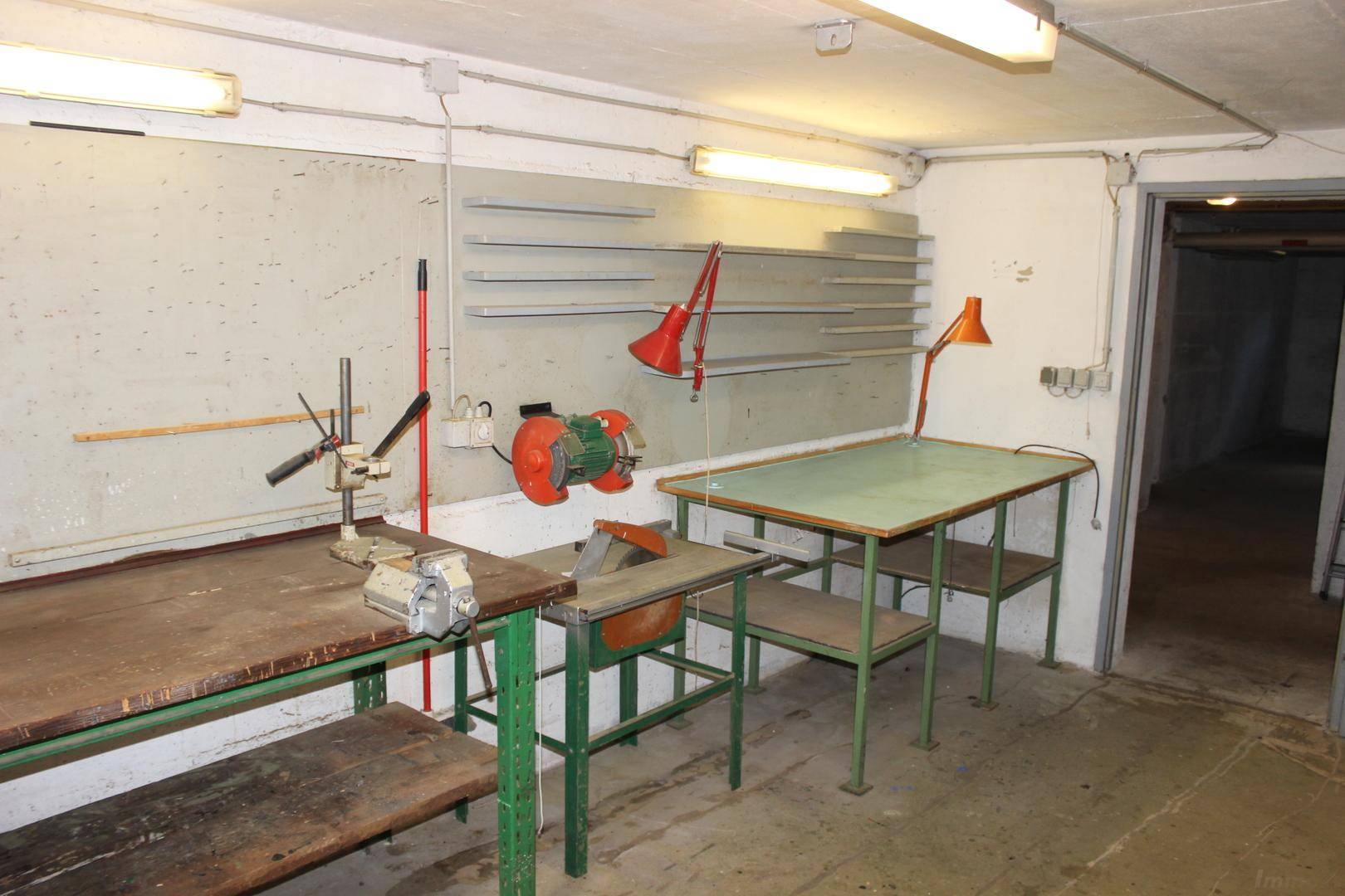 Kellerraum mit verschiedenen Werkzeugen, Regalen und Arbeitsflächen für handwerkliche Tätigkeiten.