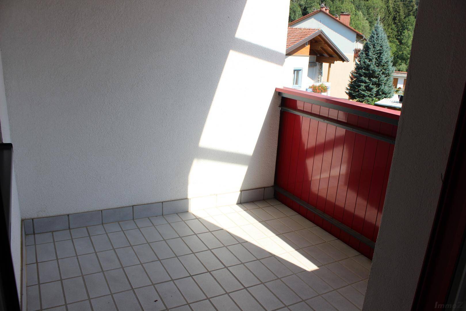 Heller Balkon mit Fliesenboden und rotem Geländer, ideal für sonnige Stunden.