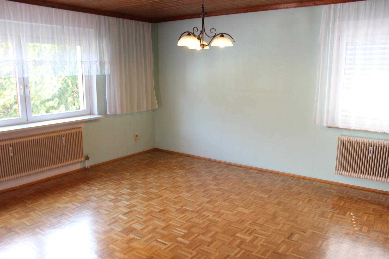 Geräumiges Zimmer mit Holzparkett, Holzdecke und zwei Fenstern für viel Tageslicht.