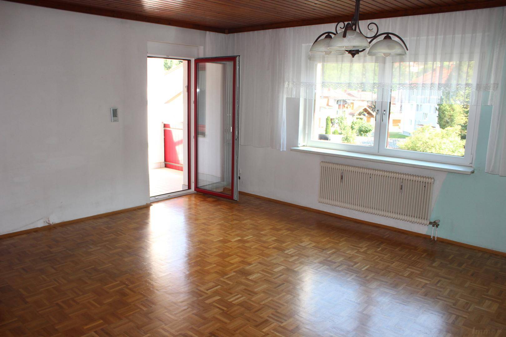 Wohnzimmer mit Parkettboden, Zugang zum Balkon und Blick auf die Umgebung.