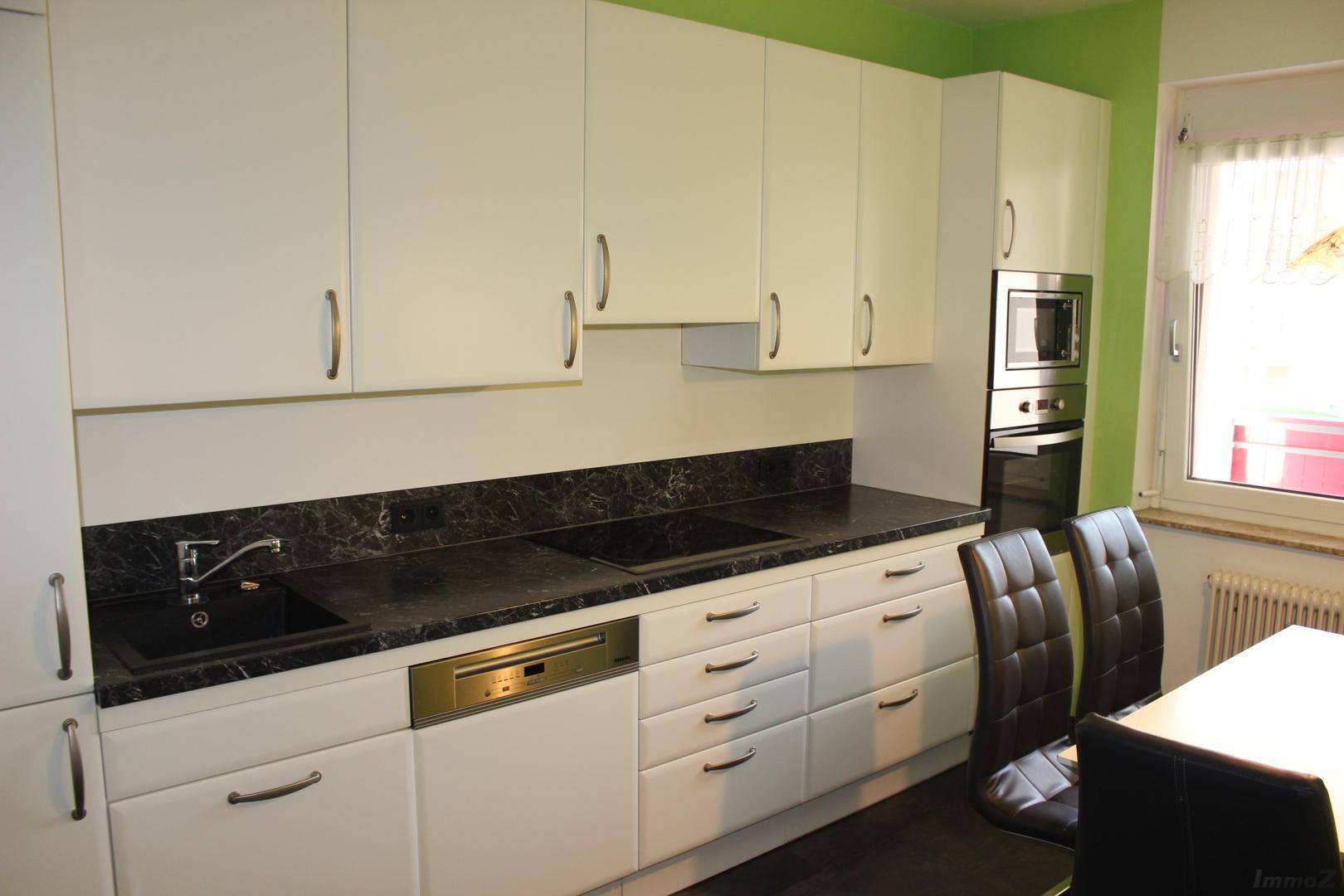 Moderne Einbauküche mit weißen Schränken, dunkler Arbeitsplatte und integrierten Geräten.