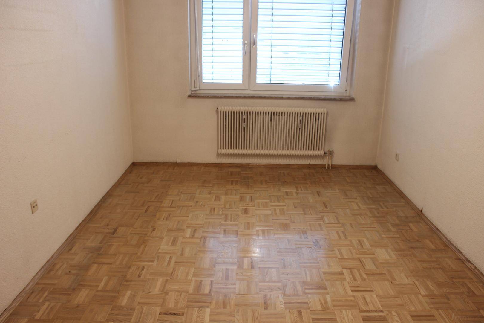 Helles Schlafzimmer mit Holzparkett und einem großen Fenster, das viel Licht hereinlässt.