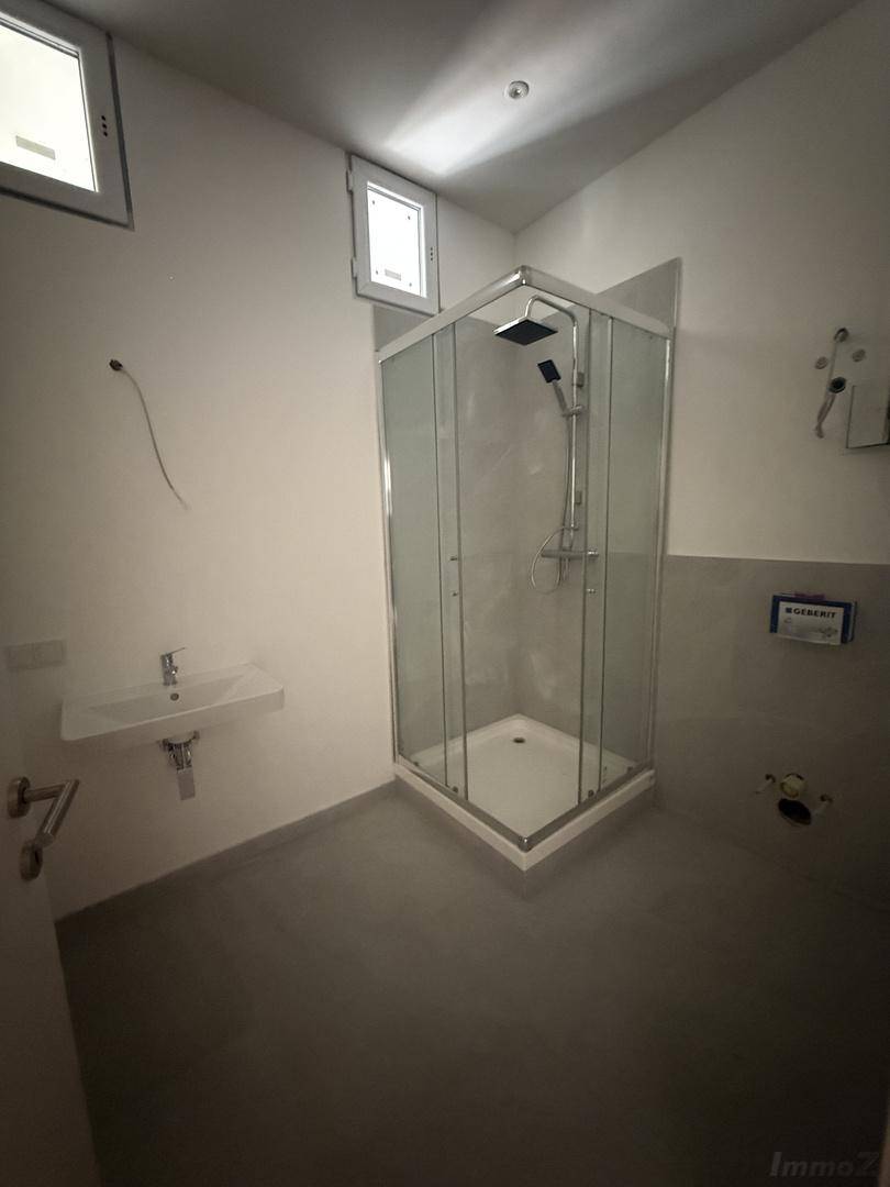 Modernes Badezimmer mit Duschkabine, Waschbecken und zwei kleinen Fenstern für Tageslicht.